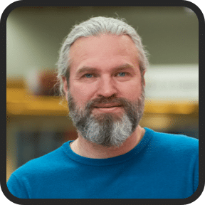 Smiling adult man with a thick grey beard and blue shirt, representing improved wellness and prostate health support from Prostadine.